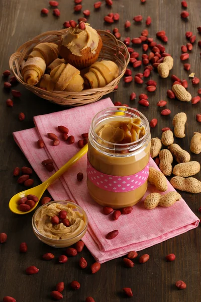 Delicious peanut butter in jar with baking on napkin on wooden table close-up — Stock Photo, Image