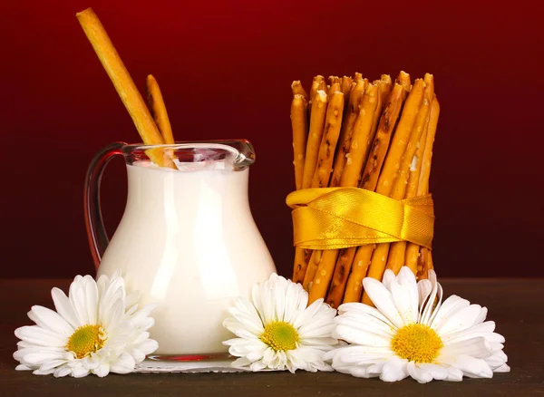 Palitos crocantes saborosos com jarro com creme de leite na mesa de madeira no fundo vermelho — Fotografia de Stock