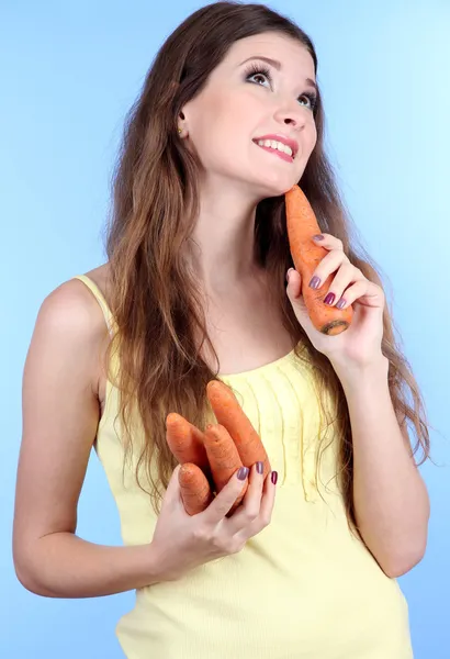 Mulher bonita com cenoura no fundo azul — Fotografia de Stock