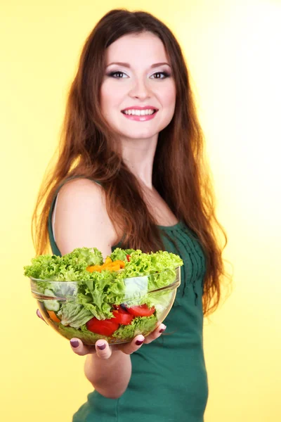 Hermosa mujer con ensalada de verduras sobre fondo amarillo — Foto de Stock