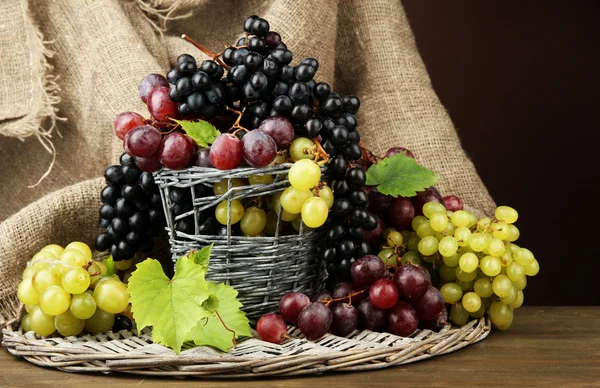 Assortment of ripe sweet grapes in basket, on brown background — Stock Photo, Image