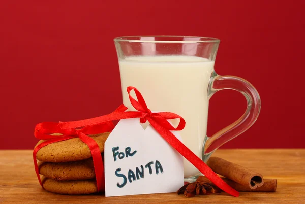 Cookie-kat a santa: fogalmi kép gyömbér cookie-kat, a tej és a karácsonyi dekoráció, piros háttér — Stock Fotó