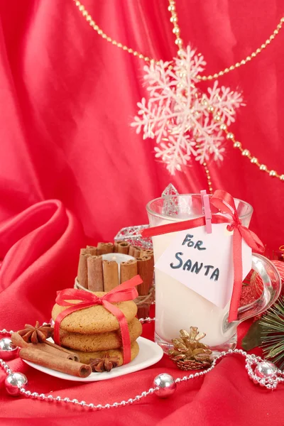 Kekse für den Weihnachtsmann: Konzeptbild von Ingwerplätzchen, Milch und Weihnachtsdekoration auf rotem Hintergrund — Stockfoto