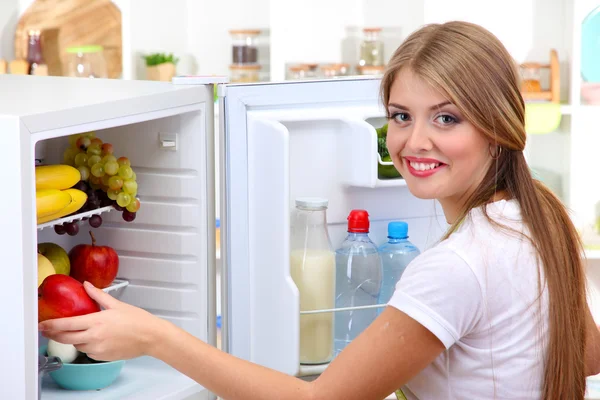 Menina jovem perto de geladeira na cozinha — Fotografia de Stock