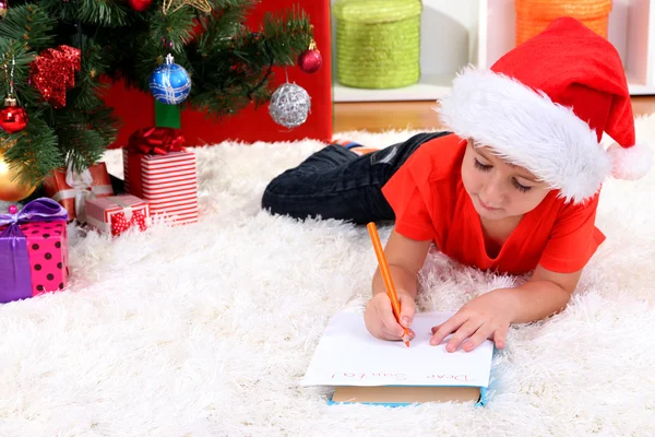 Liten pojke i santa hatt skriver brev till jultomten — Stockfoto