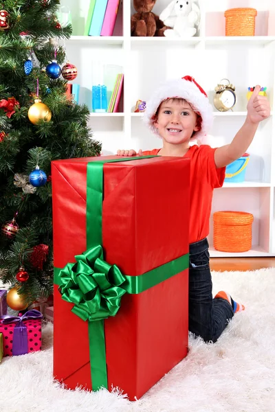 Niño en el sombrero de Santa cerca del árbol de Navidad con gran regalo —  Fotos de Stock
