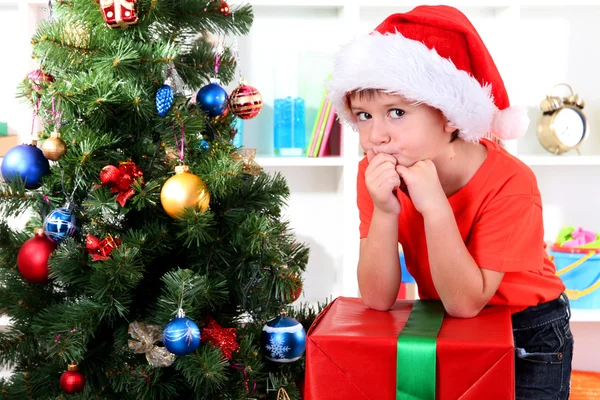 Child in Santa hat near Christmas tree with big gift Stock Picture