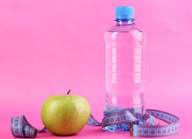 şişe su, elma ve pembe bir arka plan üzerinde ölçüm bandı