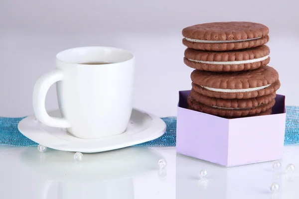 Schokoladenkekse mit cremiger Schicht und Tasse Kaffee auf violettem Hintergrund — Stockfoto