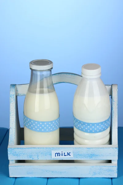 Γάλα σε μπουκάλια σε ξύλινο κουτί στον μπλε ξύλινο τραπέζι σε μπλε φόντο — Φωτογραφία Αρχείου