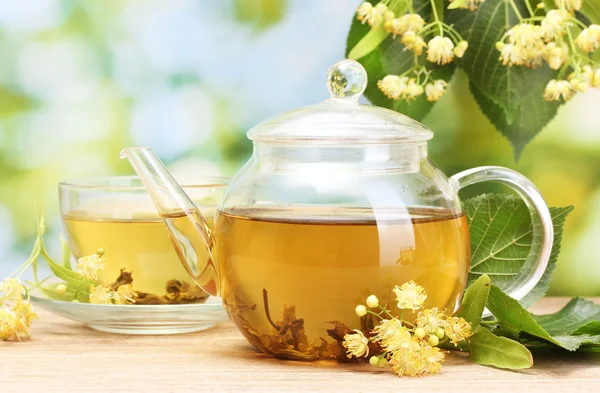 Teapot and cup with linden tea and flowers on wooden table in garden — Stock Photo, Image