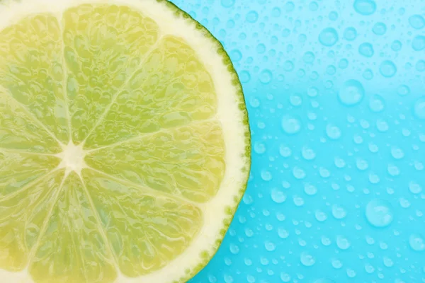 Slice of lime with drop on blue background — Stock Photo, Image