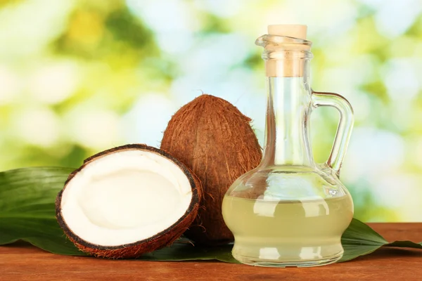 Decantador con aceite de coco y cocos sobre fondo verde — Foto de Stock