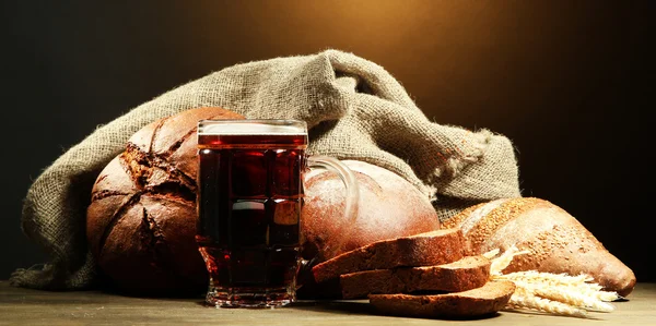 Tankard de pães de kvass e centeio com orelhas, na mesa de madeira no fundo marrom — Fotografia de Stock