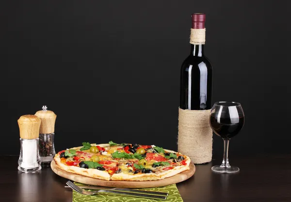 Pyszne pizze z kieliszek czerwonego wina i przyprawy na drewnianym stole na czarnym tle — Zdjęcie stockowe