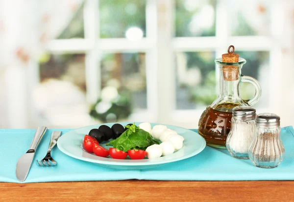 Queso mozzarella con verduras en el plato con tenedor y cuchillo en la mesa de madera — Foto de Stock