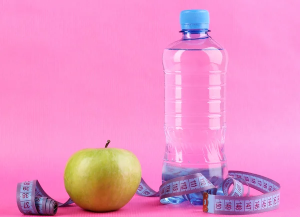 Fles water, apple en meten tape op roze achtergrond — Stockfoto