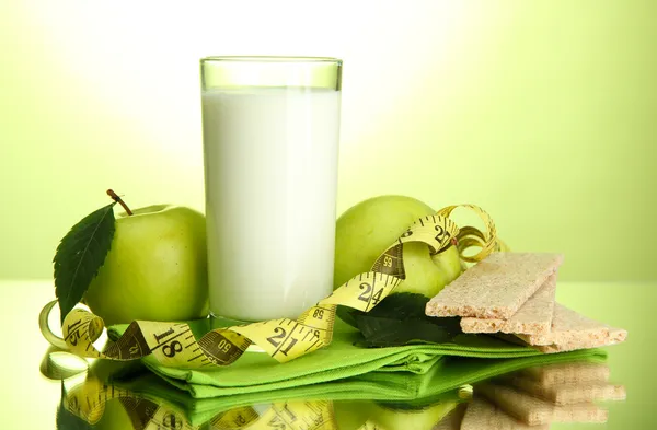 Verre de kéfir, pommes, pains croustillants et ruban à mesurer, sur fond vert — Photo