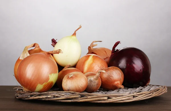 Ripe onions on wicker cradle on wooden table on grey background — Stock Photo, Image