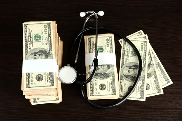 Healthcare cost concept: stethoscope and dollars on wooden background — Stock Photo, Image