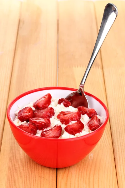 Hüttenkäse in roter Schüssel mit Erdbeeren in Scheiben auf Holztisch — Stockfoto