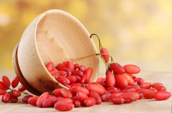 Ripe barberries in wooden bowl, on table, on yellow background — Stock Photo, Image