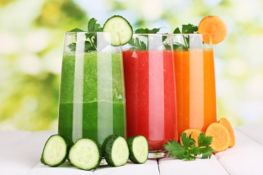 Fresh vegetable juices on wooden table, on green background clipart