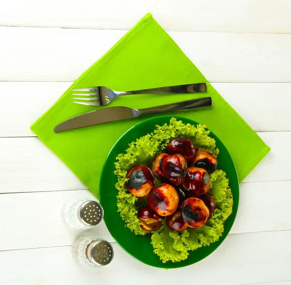Roasted chestnuts with lettuce in the plate on white wooden background — Stock Photo, Image