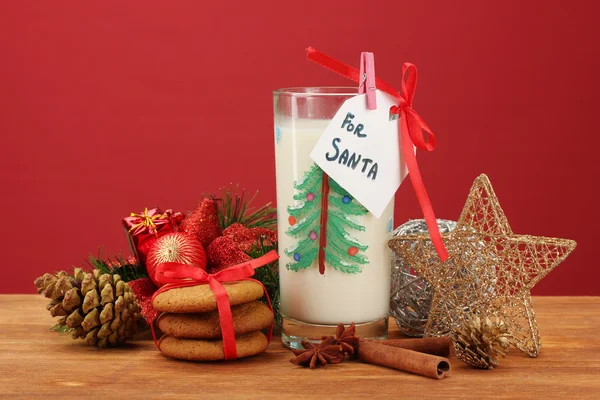 Pliki cookie dla santa: koncepcyjnego obrazu imbir ciasteczka, mleko i Bożego Narodzenia ozdoba na czerwonym tle — Zdjęcie stockowe