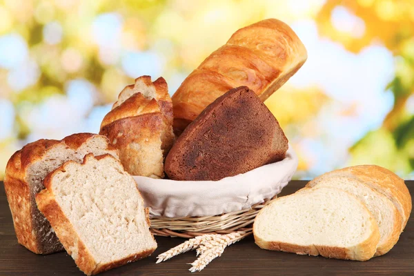 Pane fresco in cesto su tavolo in legno su sfondo naturale — Foto Stock