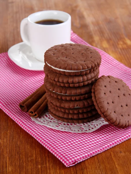 Chocolate cookies with creamy layer and cup of coffe on wooden table close-up — Stock Photo, Image