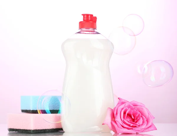 Líquido de lavagem de pratos com esponjas e flores sobre fundo rosa — Fotografia de Stock