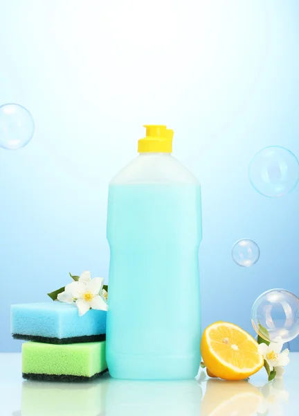 Dishwashing liquid with sponges and lemon with flowers on blue background — Stock Photo, Image