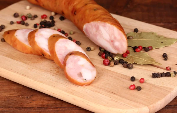 Tasty sausage on chopping board on browm background — Stock Photo, Image