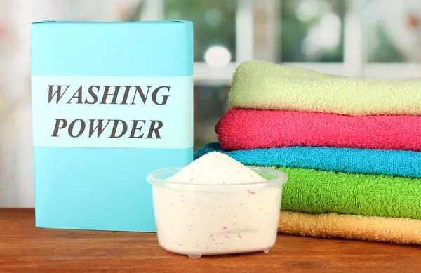 Box of washing powder with blue measuring cup and towels, on wooden table close-up — Stock Photo, Image