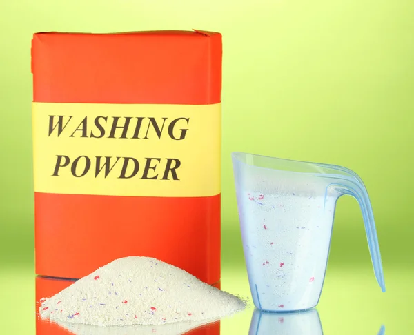 Box of washing powder with blue measuring cup, on green background close-up — Stock Photo, Image