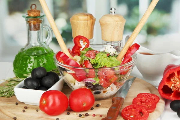 Salada grega fresca em taça de vidro cercada por ingredientes para cozinhar em mesa de madeira no fundo da janela — Fotografia de Stock