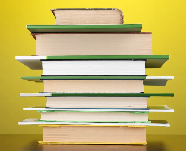 Stapel interessante boeken en de tijdschriften op houten tafel op gele achtergrond — Stockfoto