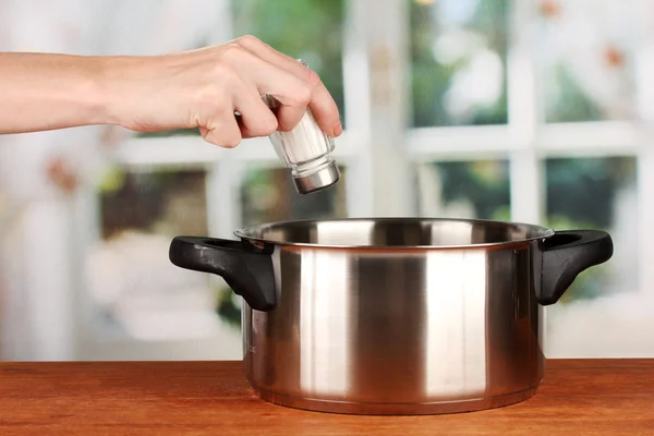 Hand adding salt using salt shaker on bright background — Stock Photo, Image