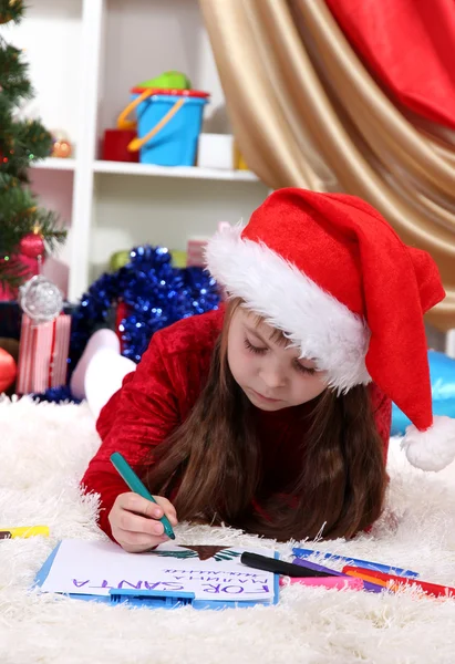 Menina bonita escreve carta ao Papai Noel em quarto festivamente decorado — Fotografia de Stock