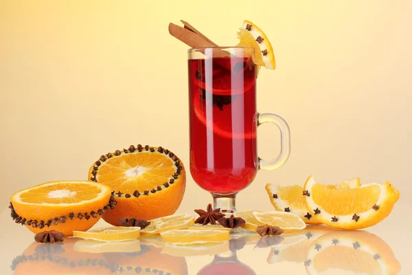 Fragrant mulled wine in glass with spices and oranges around on yellow background — Stock Photo, Image