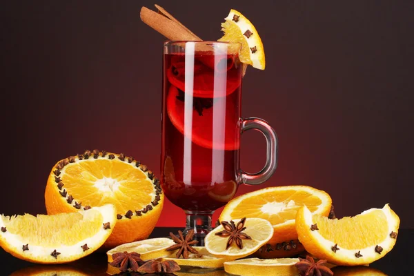 Fragrant mulled wine in glass with spices and oranges around on red background — Stock Photo, Image