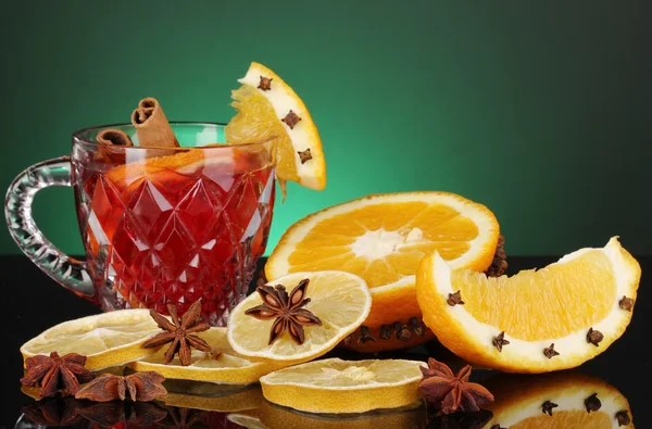 Fragrant mulled wine in glass with spices and oranges around on green background — Stock Photo, Image
