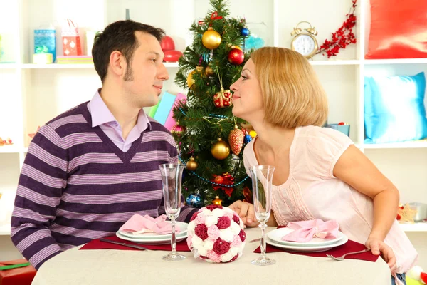 Joven pareja feliz sosteniendo copas con champán en la mesa cerca del árbol de Navidad —  Fotos de Stock