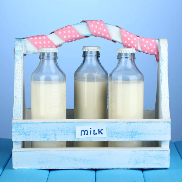Mleko w butelkach w drewniane pudełko na niebieskim drewnianym stole na niebieskim tle — Zdjęcie stockowe