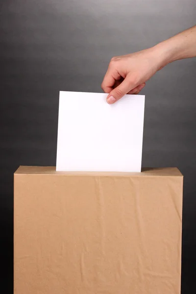 Mão com cédula de voto e caixa em fundo cinza — Fotografia de Stock