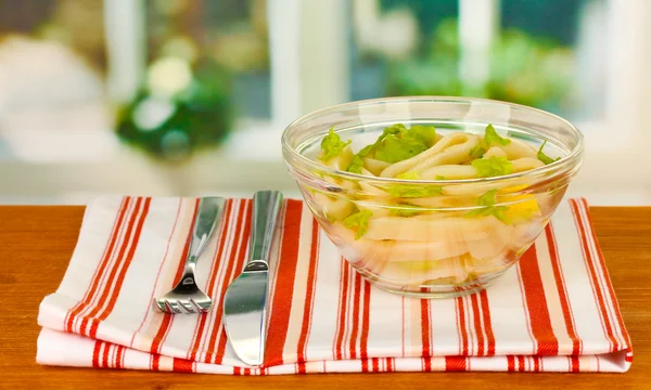 Салат из колец кальмара, лимона и салата в стеклянной миске на деревянном столе крупным планом — стоковое фото