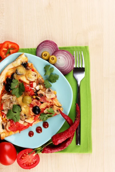 Délicieuse tranche de pizza sur plaque de couleur avec des ingrédients autour de gros plan sur une table en bois — Photo