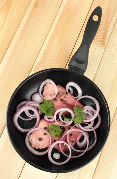 A pieces of pork with onions fried in pan on wooden table — Stock Photo, Image
