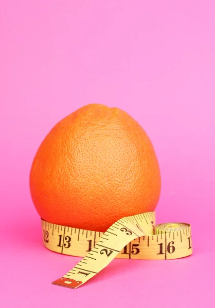 Orange with measuring tape on pink background — Stock Photo, Image